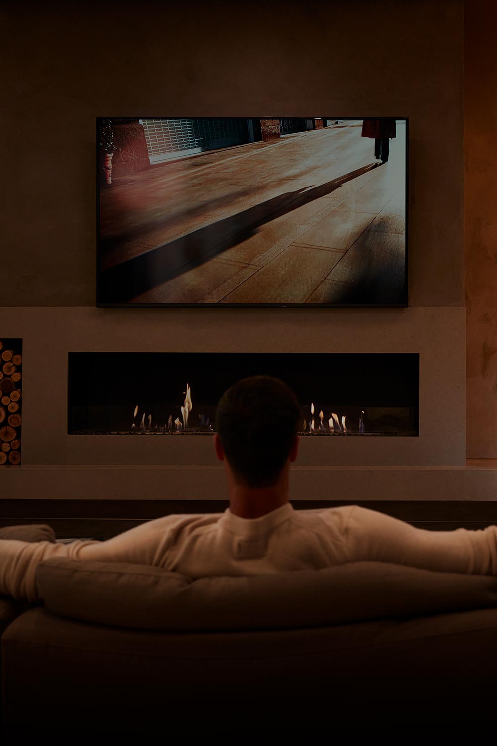 Person watching television above a fireplace in a dim living room
